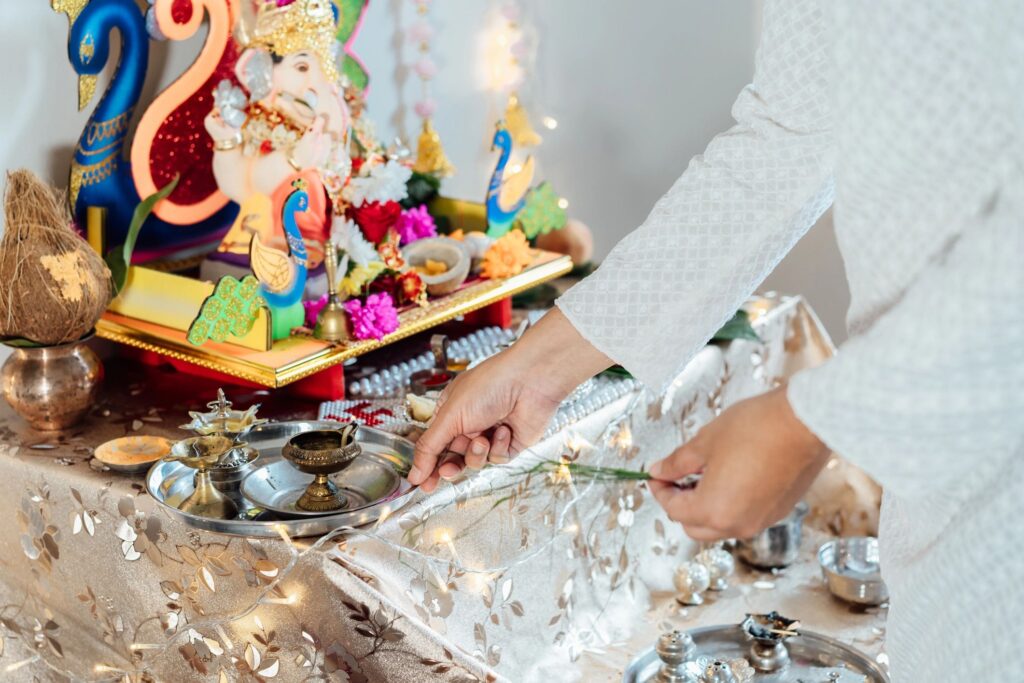 Close up Indian man dressed in traditional wear engages in worship at home altar, adorned with decors and offerings for god Ganesh during festive celebration. Indian culture, hindu ritual and customs